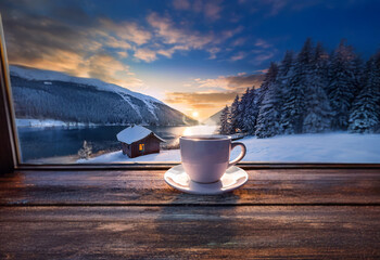 Poster - A white coffee cup sits on a windowsill overlooking a snowy mountain landscape with a lake and a small cabin.