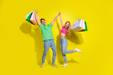 Full body portrait of two nice young partners hold hands bags isolated on vibrant yellow color background