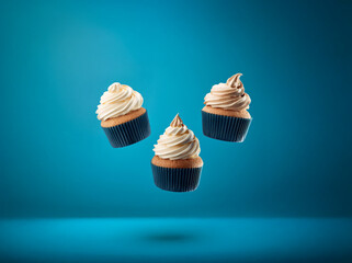 Poster - Three cupcakes with swirls of white and beige frosting, floating in mid-air against a blue background.