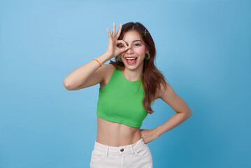 Beautiful young Asian woman with healthy and perfect skin shows OK signal isolated on blue background.