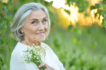 Wall Mural - Portrait of a beautiful elderly woman with a bouquet of flowers in the park