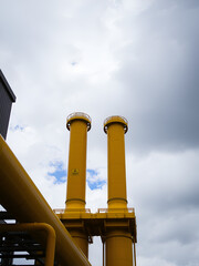 Two Large Yellow Industrial Pipes Against a Cloudy Sky