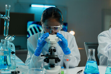 Wall Mural - scientist is using a microscope, carefully examining samples in a modern, blue lit laboratory