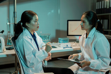 Wall Mural - two young female scientists are discussing research in a laboratory at night, with one holding a pen