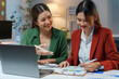 ©  NCST Studio - Two young businesswomen are working late in the office, collaborating on a project and analyzing financial data on a laptop