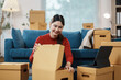 ©  NCST Studio - Young woman is unpacking cardboard boxes in her new apartment, she is smiling and looking inside a box