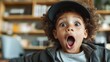© Dulemegapixel - A surprised looking child wearing a cap, with wide-open eyes and mouth, in an indoor setting with a bookshelf in the background, showcasing a lively expression.