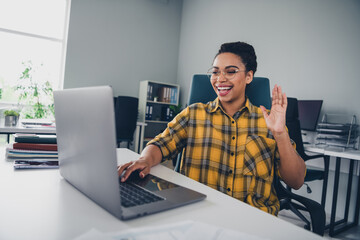 Photo of young woman work netbook video call wave hand wear yellow plaid shirt comfortable modern office room interior indoors workspace