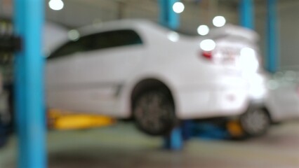 Blurred image of white car being serviced in auto repair shop. Automobile maintenance and repair.