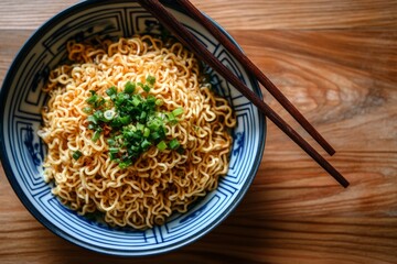 A bowl filled with instant noodles is garnished with chopped green onions, accompanied by a pair of chopsticks resting on the side, all set on a wooden tabletop