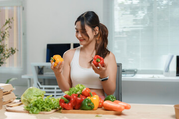 Young woman is smiling while choosing between a red and a yellow bell pepper for her salad, in her home office