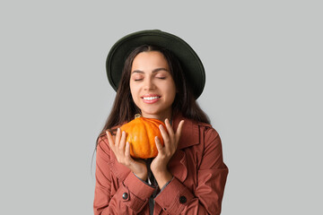 Stylish young woman with fresh pumpkin on grey background