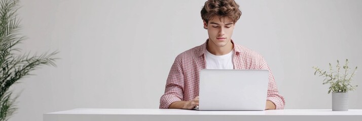 Leinwandbilder - A dedicated young freelancer is engaged in remote work at a laptop in a bright, minimalist environment with green plants. Generative AI