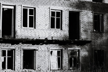 Poster - A black and white photo of an old abandoned building with cracked walls and overgrown vegetation.