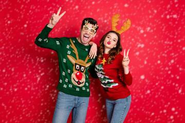 Portrait of crazy two family people wife husband brown hair lean shoulder make v-signs send air kiss lips pouted wear funny antler christmas tree clothes eyeglasses isolated over red color background