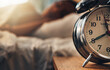 © Courtney Haas/peopleimages.com - Alarm clock, table and person sleeping, relax and resting in bedroom for energy or lazy at home. Time, bed and oversleeping with fatigue, morning and tired on comfortable mattress for peace or calm