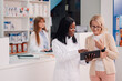 © Zamrznuti tonovi - Diverse pharmacy shop worker with tablet explaining to senior woman.