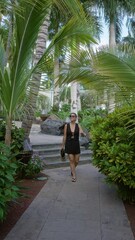 Sticker - Young woman enjoying a stroll outdoors in lanzarote, canary islands, surrounded by lush tropical greenery and palm trees wearing black dress and sunglasses