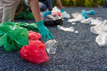 Close-up of female hands from a family collecting plastic waste and bottles from the ground. They wear gloves and focus on recycling to help reduce plastic pollution and protect the environment.