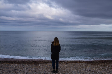 Mujer joven que se siente sola y triste  o pensativa o esperando. mirando el mar en un día sombrío , Young woman feeling alone and sad or thoughtful or waiting. looking at the sea on a gloomy day