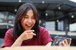 © M Alfan Setyawan - attractive asian woman excited using smartphone to playing game online with pointing finger at screen sitting in cafe, low angle view