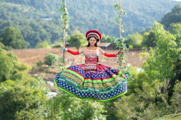 A woman in vibrant traditional clothing swings outdoors in a lush green landscape, celebrating culture and nature in harmony.