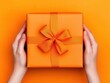 © Thann - Hands securely tying a bow around an orange gift box on a vibrant background celebrating the art of present wrapping