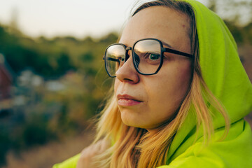 A person wearing a bright hoodie and glasses poses confidently outdoors amidst a soft, blurred background in autumn