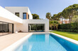 © JuanM - Modern villa with a swimming pool surrounded by lush greenery in bright daylight