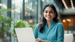 © colnihko - Confident professional Indian woman working on laptop in modern office setting