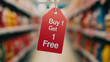 © Cheetose - Buy 1 Get 1 Free sale tag hanging in store aisle, showcasing promotional offer that attracts shoppers. vibrant red tag stands out against blurred background of products