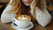 © Aventurine - Cozy scene of woman with long red hair resting her chin on her hand, gazing at beautifully crafted latte art in white cup on wooden table. warm atmosphere invites relaxation and enjoyment