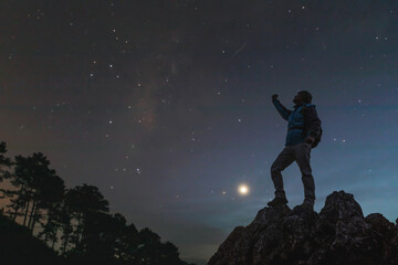 Wall Mural - silhouette of guy with backpack raised up arm on top hill, sky with stars, space landscape with milk