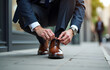 © Marina - Man in a suit tying brown leather shoes while crouching on the city sidewalk