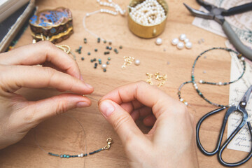 Woman making handmade gemstone jewelry. Beads  and tools on wooden table. Top view with woman hands.