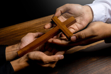 Man holding a religion cross together on wooden background. Symbol of faith and worship in God. People christianity prayer in church