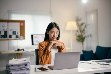 Poster - Young businesswoman is sitting at her desk and working on a laptop, she is smiling slightly and appears to be focused on her task