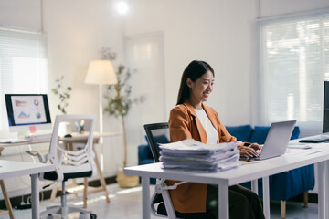 Poster - Young professional woman is working from her computer in her bright and modern office. She is smiling as she types on her laptop