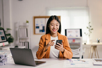 Poster - Cheerful businesswoman working on a project in a modern office, using a smartphone to analyze data and browse online