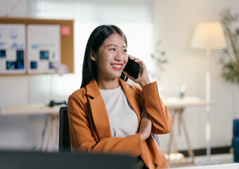 Poster - Asian businesswoman happily talking on her phone at her desk in a corporate office, exuding confidence and dedication