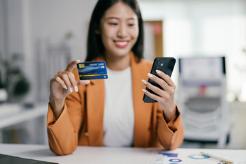 Asian businesswoman happily shopping online with a credit card and smartphone, showcasing seamless digital transactions in business and finance