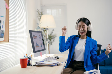 Businesswoman is having fun in her office, listening to music with headphones and dancing while taking a break from working on a computer