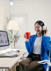 Poster - Young businesswoman wearing headphones, listening to music and drinking coffee during a short break at her desk in a modern office