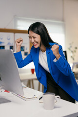 Poster - Young businesswoman is raising her arms in front of her computer, she is happy and celebrating a business achievement
