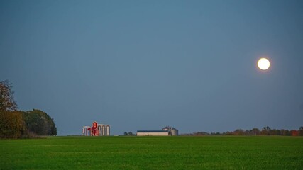 Wall Mural - Full moon rising above farmland with fields and buildings, time lapse view