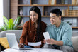 © Liubomir - Asian couple managing finances in cozy living room with laptop and documents. Man and woman discussing financial planning and budgeting, teamwork on laptop fostering positive communication.