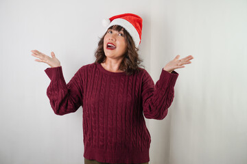 Excited young asian woman wearing santa clause hat and red long sleeved sweater is pointing copy space beside her, isolated over white background. Concept for Christmas Holiday and New Year Party