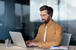 © Liubomir - Mature businessman wearing headset engaged in video conference at office. Confident professional using laptop for online communication, showcasing skills in remote work and digital collaboration.