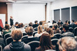 © kasto - Speaker giving a talk in conference hall at business event. Rear view of unrecognizable people in audience at the conference hall. Business and entrepreneurship concept