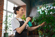 © Юлия Завалишина - Running of own business. Young woman florist with spray bottle watering fertilizing plants in botanical store. Small business owner working at flower shop smiling surrounded by plants Small business